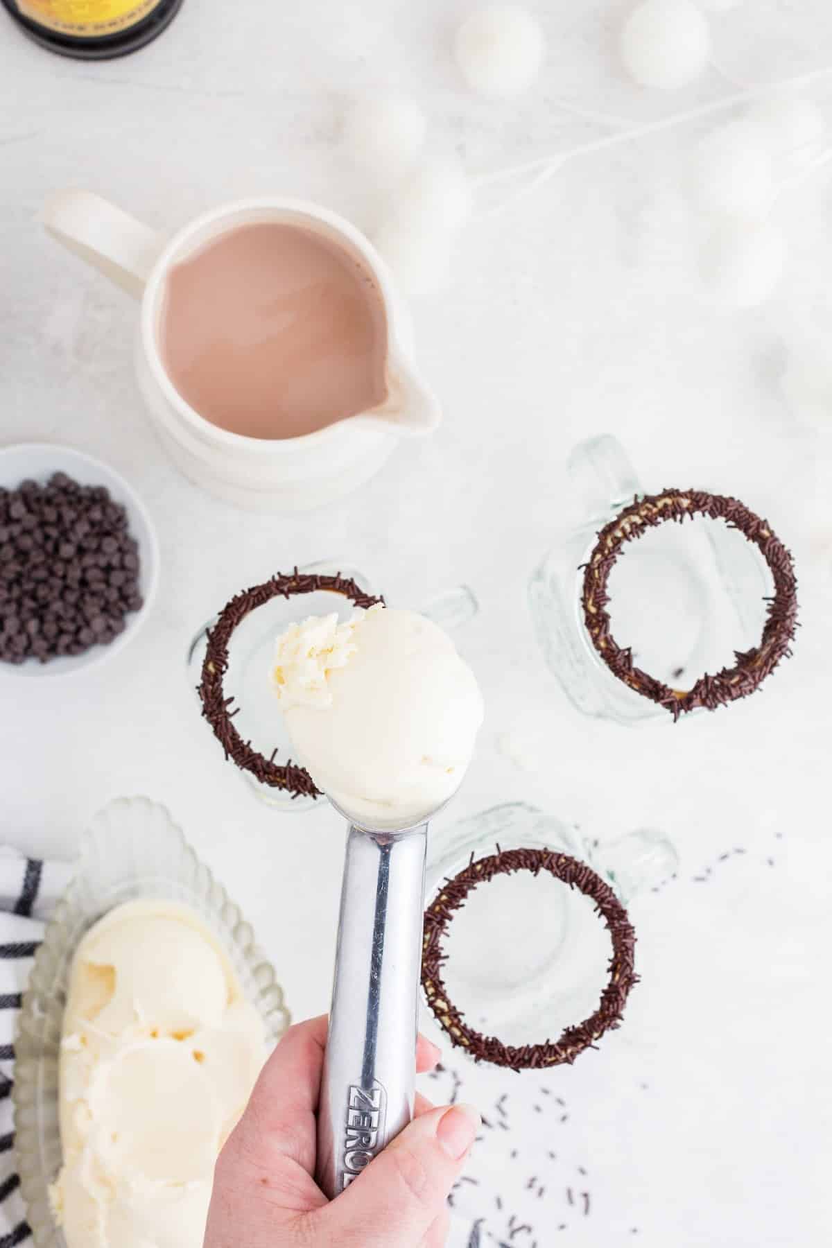 Coating three glasses with chocolate covered rim with sprinkles and putting a scoop of ice cream into each glass.