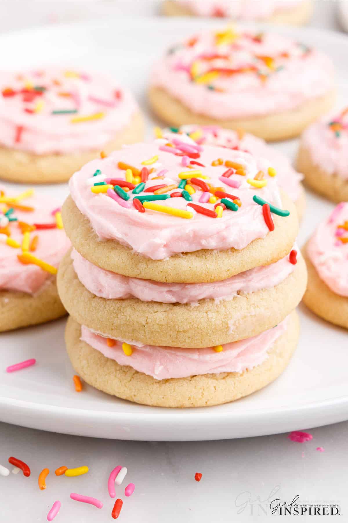 A stack of soft and chewy sugar cookies with pin frosting and colorful sprinkles.