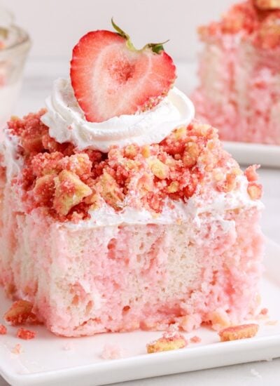 Close up of a slice of Strawberry Crunch Poke Cake showing the marbling colors and garnish, with other pieces of cake in the background.