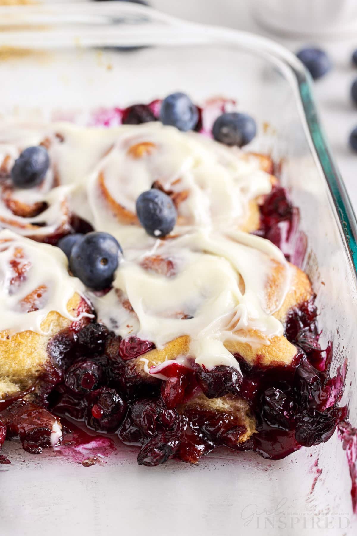 Pan filled with Blueberry Cinnamon Rolls with frosting and fresh blueberries on top.