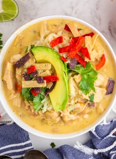 Large bowl of Green Chicken Chili with garnish on top of cilantro, avocado, tortilla strips, with text overlay.