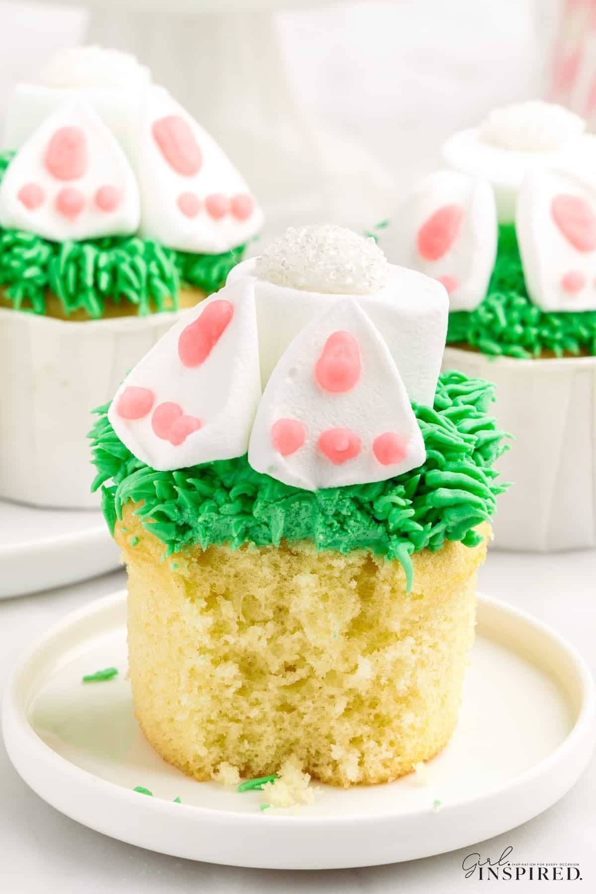 View of Bunny Butt Cupcakes on a platter showing the underside of the bunnies feet, with other cupcakes in the background.