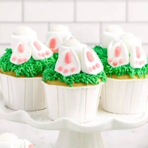 View of Bunny Butt Cupcakes on a platter showing the underside of the bunnies feet, with other cupcakes in the background and text overlay.