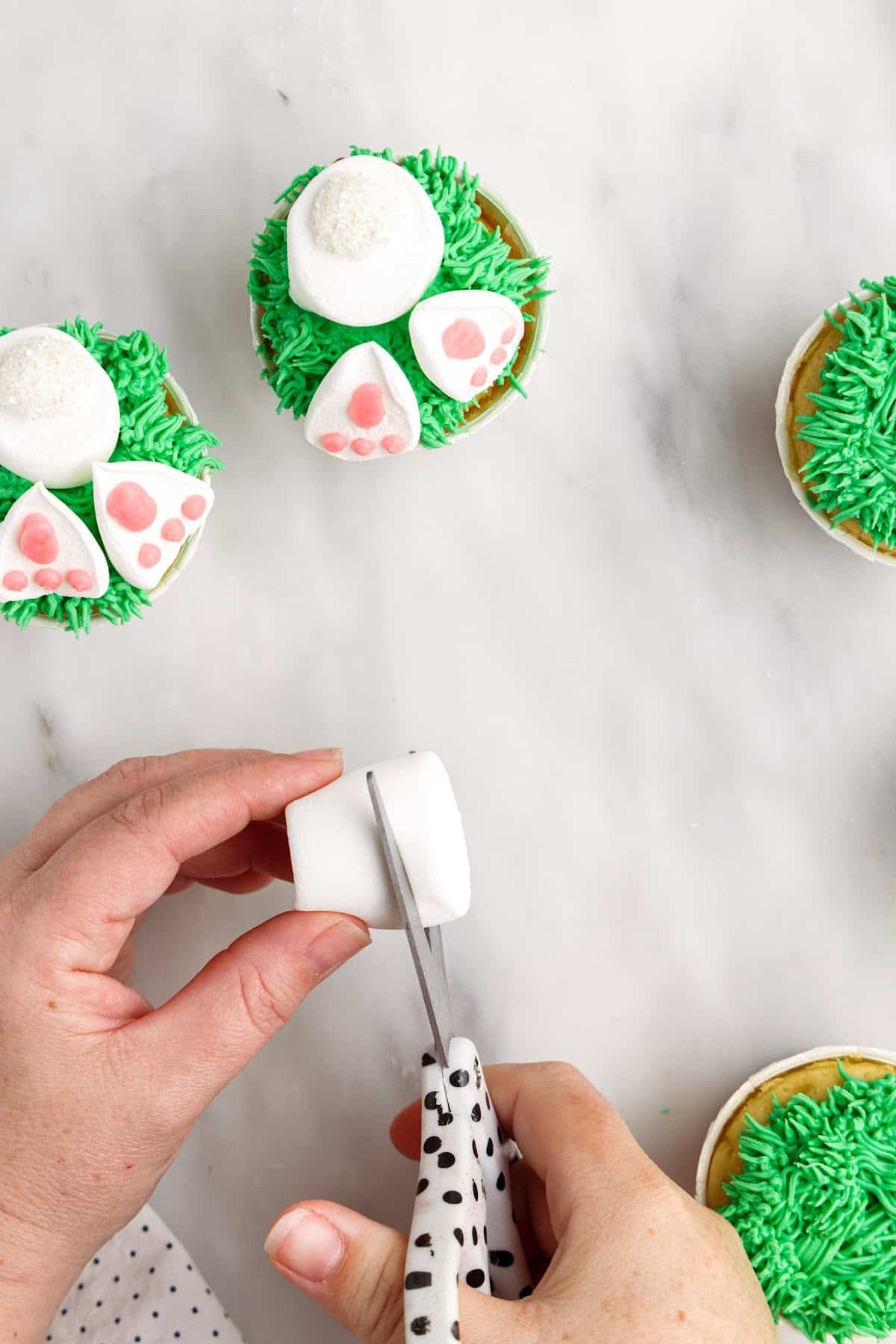 Cutting marshmallows into smaller pieces for the bunny butt, cupcakes off to the side that are partially decorated.