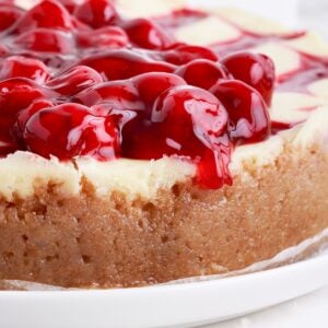 Side view of the Cherry Cheesecake showing the graham cracker crust, cheesecake filling and cherries oozing over the side.
