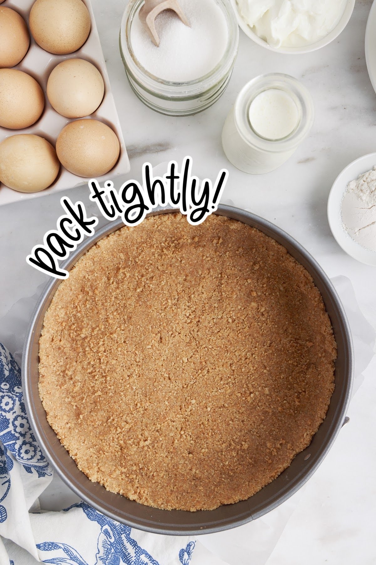 Graham cracker crust pressed into the bottom and sides of a springform pan, with other ingredients in the background.