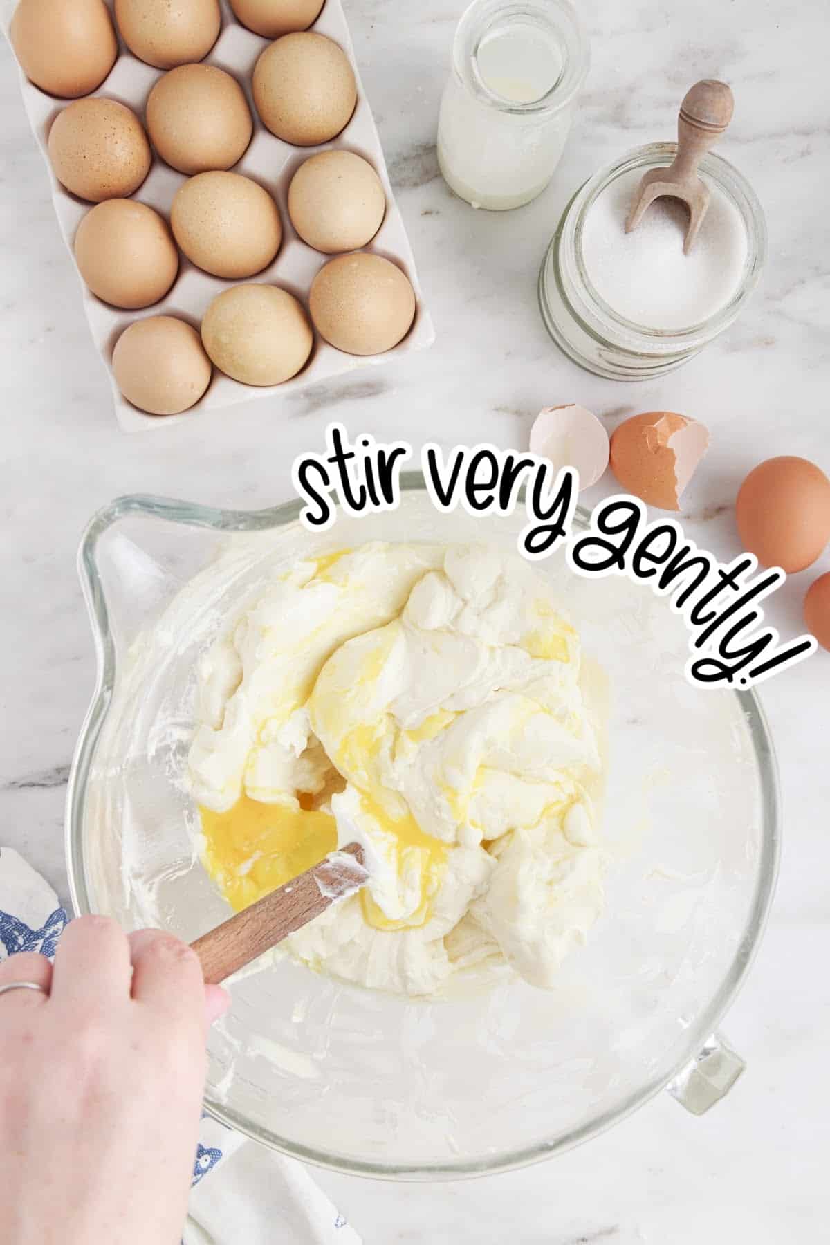 Mixing in the eggs one at a time into the cheesecake batter, with other ingredients in the background.