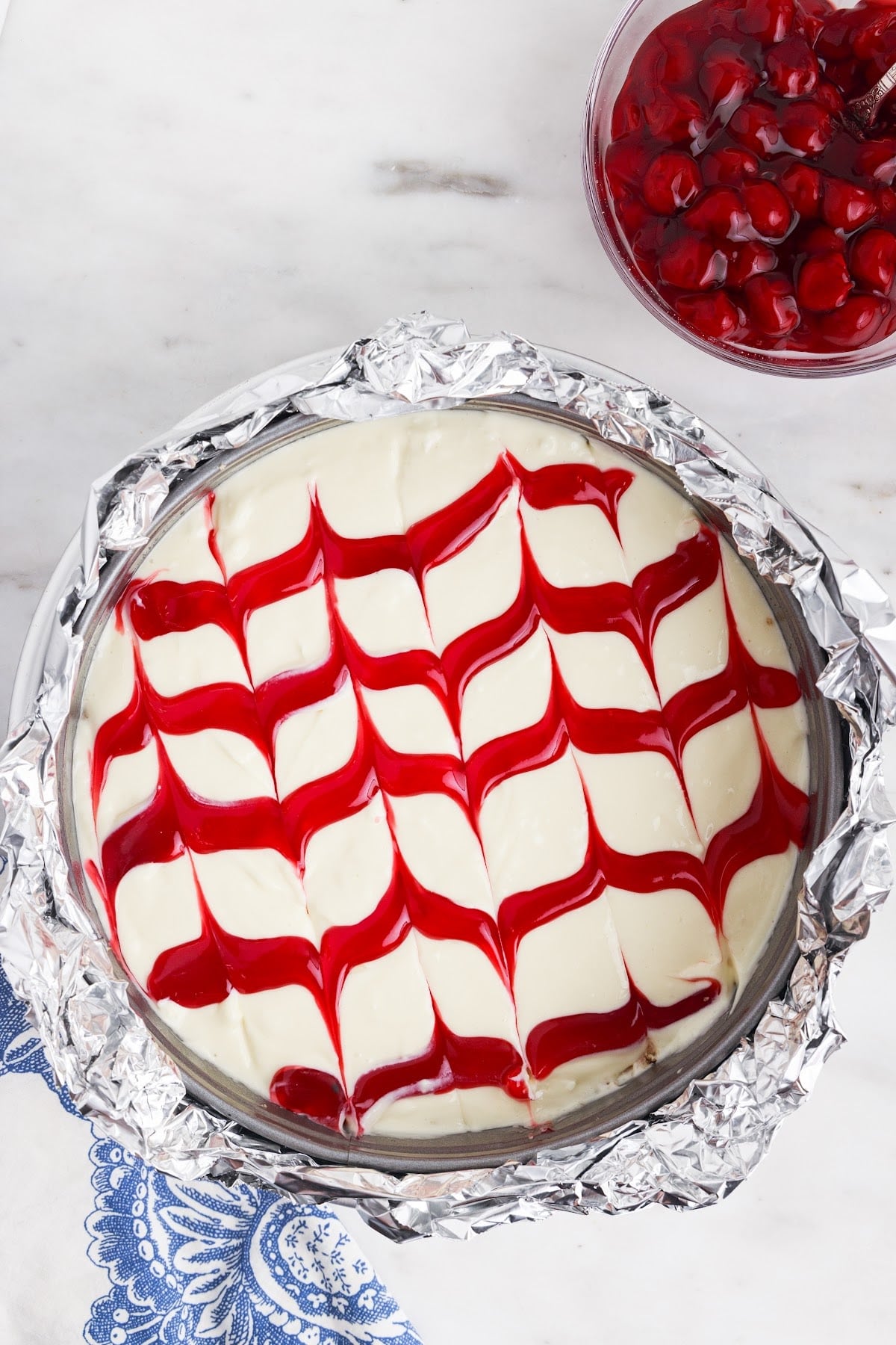 Foil wrapped springform pan, ready to back in a water back, with cherries in the background.