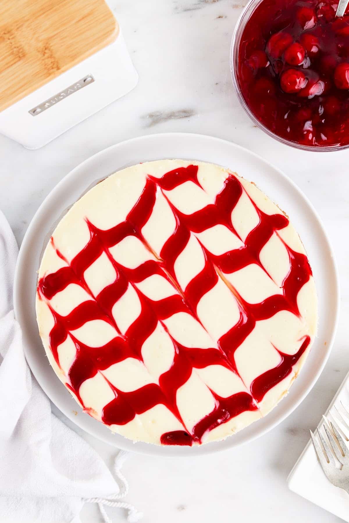 Fully baked cherry cheesecake, with cherry sauce decorated on the top, with cherries in the background.