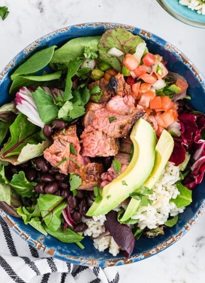 Sliced Chipotle Steak on a salad with slices of avocado.