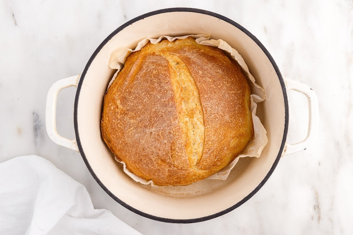 Fully baked bread sitting in the Dutch oven surrounded with parchment paper.