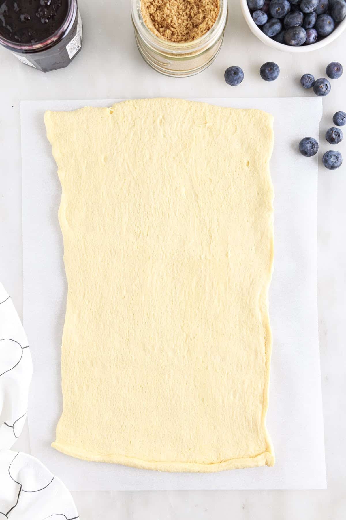 Rolled out dough into a rectangle on parchment paper. with ingredients in the background.