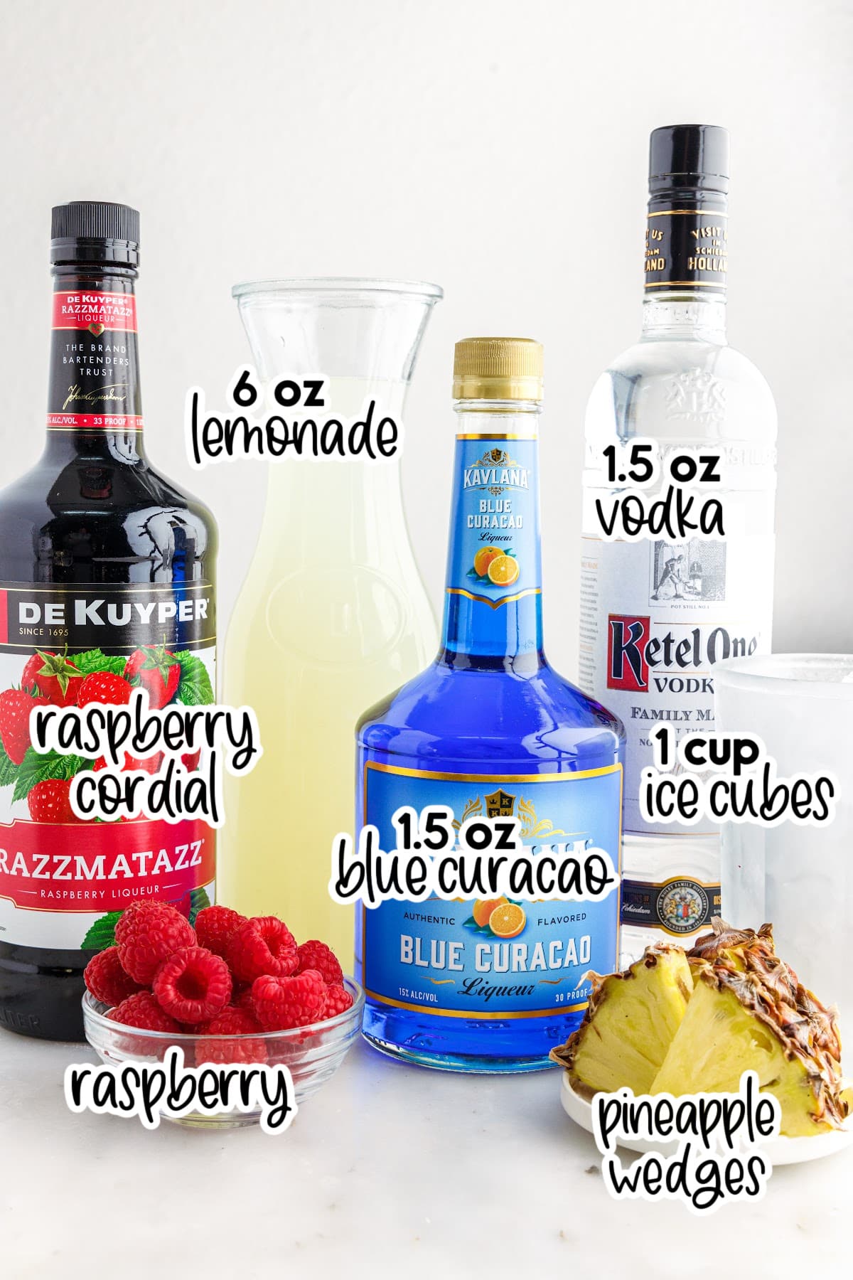 All ingredients to make this Fruit Tingle Drink on the counter, in their own alcohol bottles, bowls of fruit, and a pitcher in the back ground.