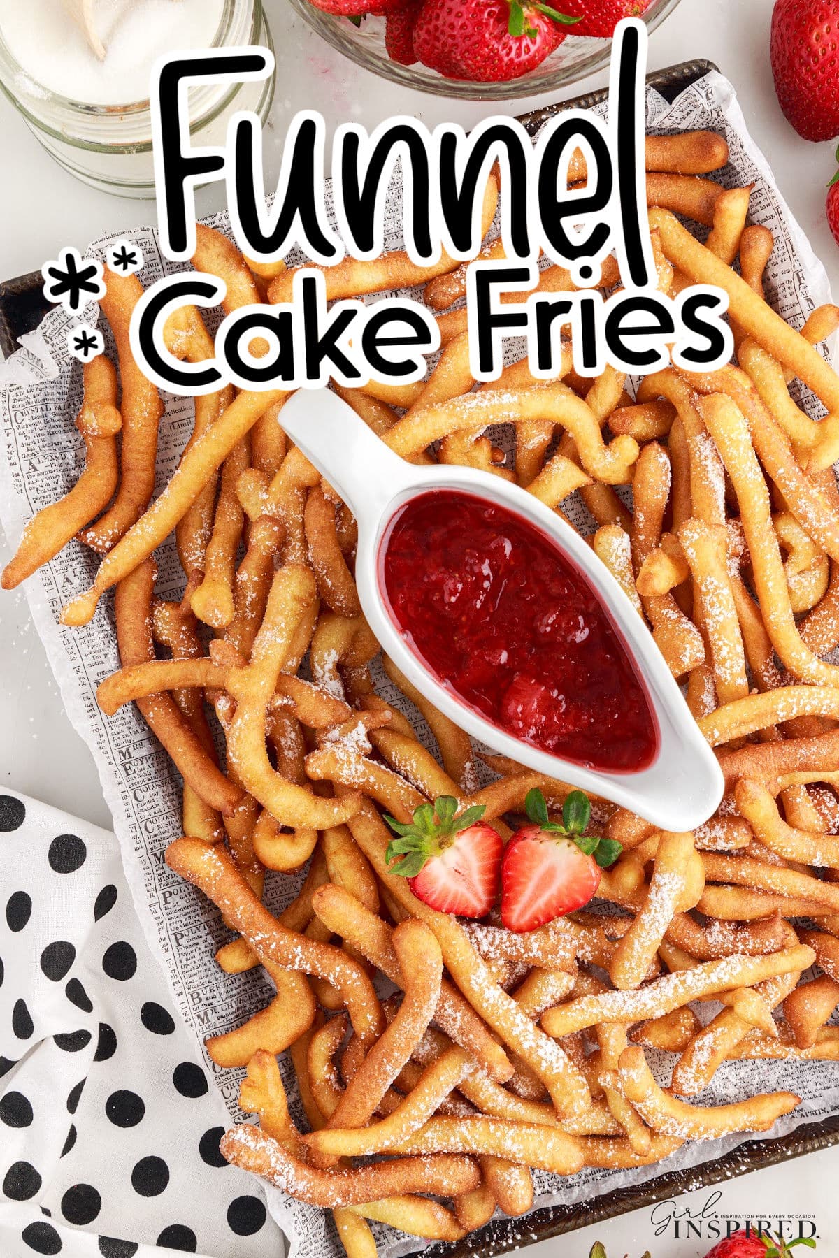 A large tray of Funnel Cake Fries on newsprint paper with a dish of strawberry sauce.