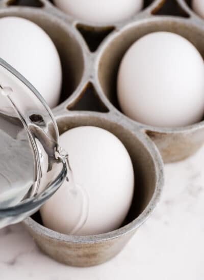 Hard-Boiled eggs in the oven being made by filling each muffin tin 1/2 with water and an egg in each.