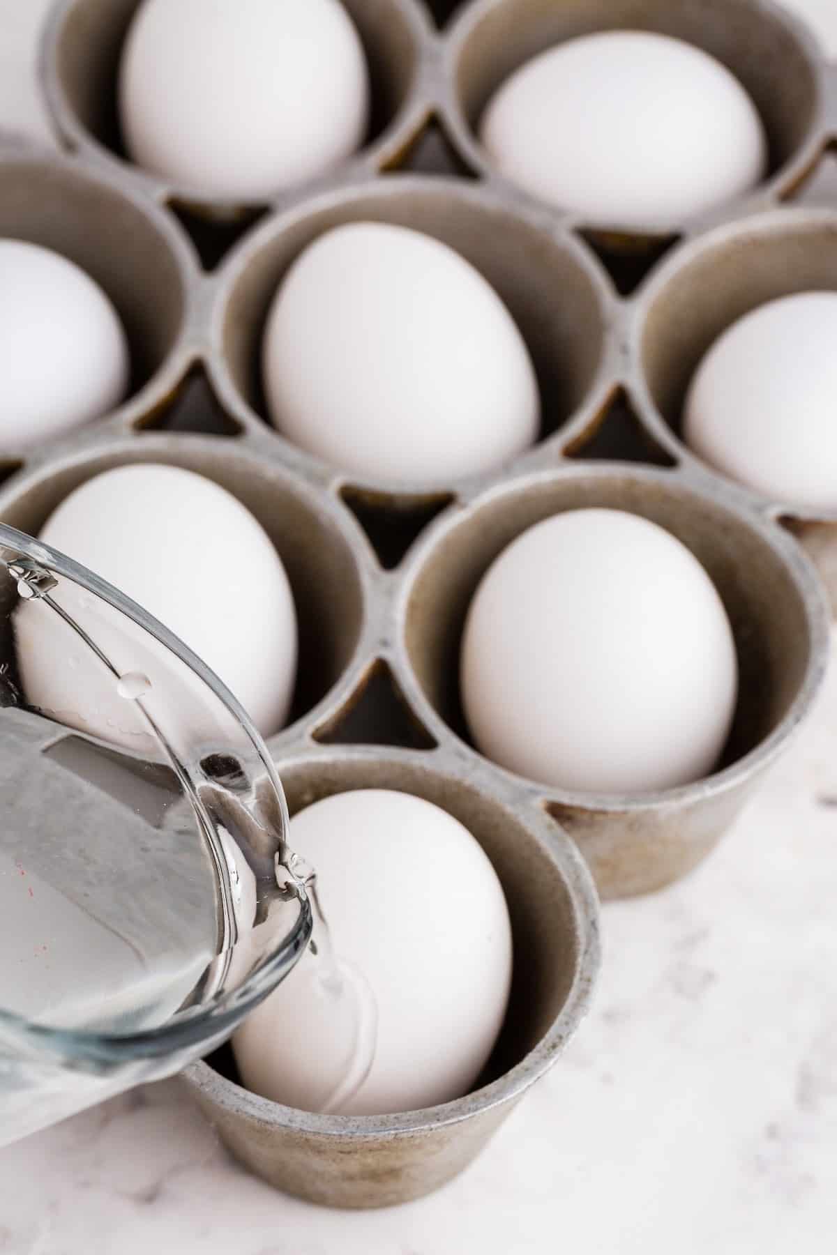 Pouring water into each muffin tin space around each egg.