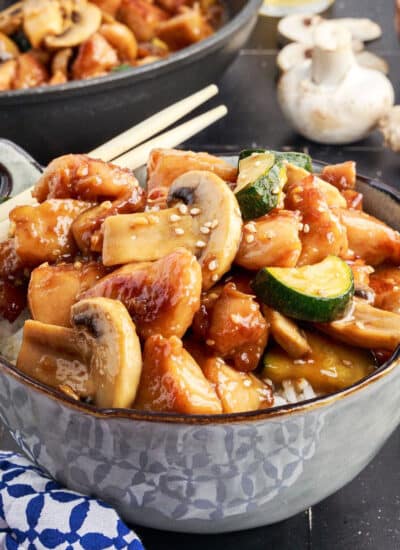 Bowl of Panda Express Mushroom Chicken with chop sticks resting on the side of the bowl, with a full skillet of the meal in teh background.