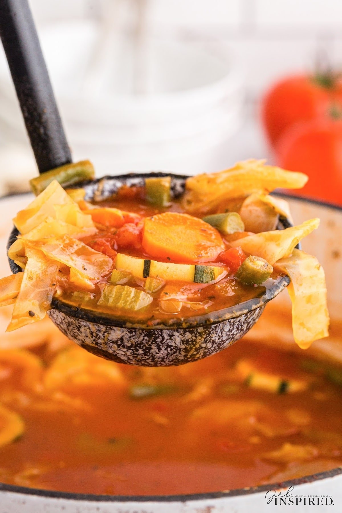 Large ladle of Diet Cabbage soup resting above the pot of soup, showing the ingredients in the photo.