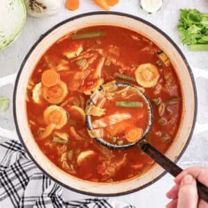 Large pot filled with Diet Cabbage Soup, a ladle spooning out a scoop of soup loaded with veggies, and text overlay.