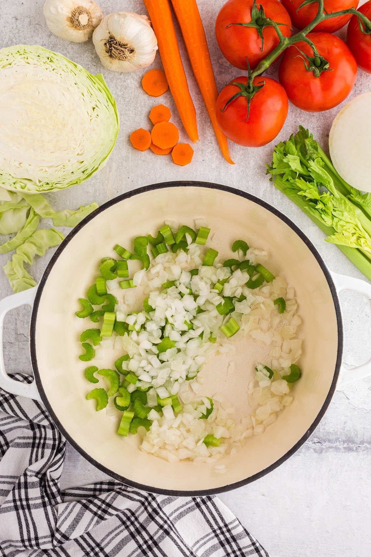 Diced veggies in a pot on the stove, stirring and sauteing, with other ingredients in the background for this soup.
