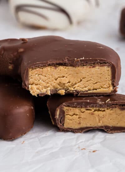 Side view of Peanut Butter and Chocolate Eggs and Bunnies parchment paper on the counter, cut in half showing the inside peanut butter, with other chocolate covered eggs in the background.