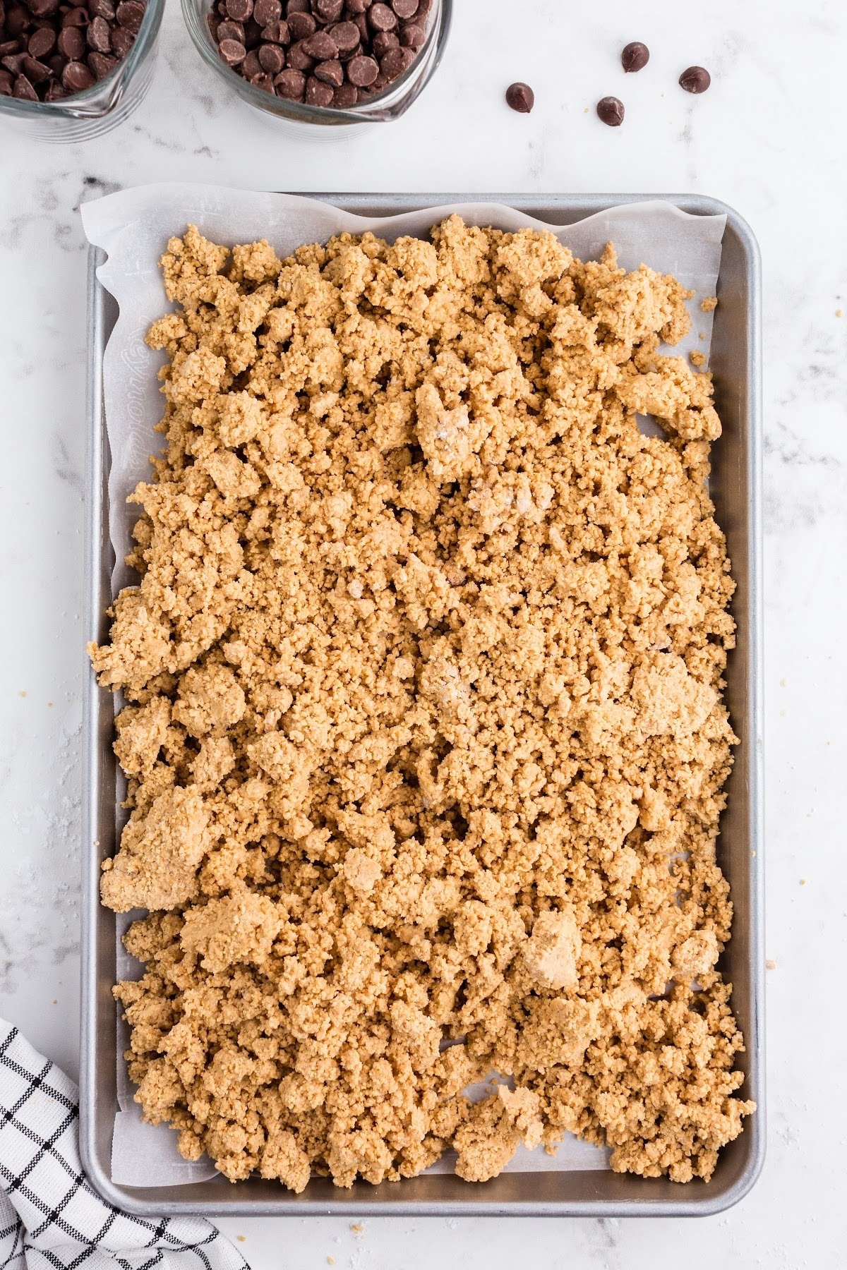 Put the peanut butter mixture into the sheet pan, with chocolate chips in the background.