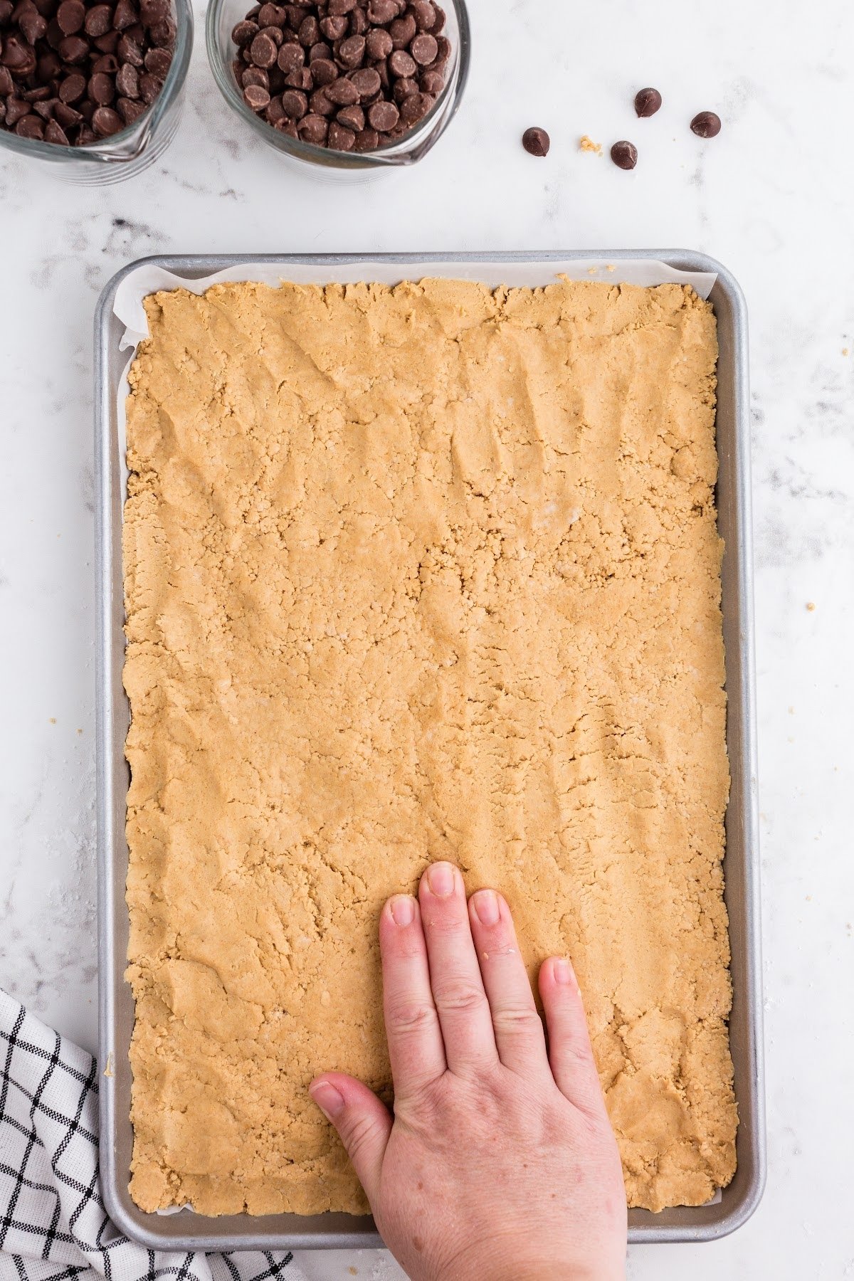 Press the peanut butter mixture into the sheet pan until evenly spread, chocolate chips in the background.