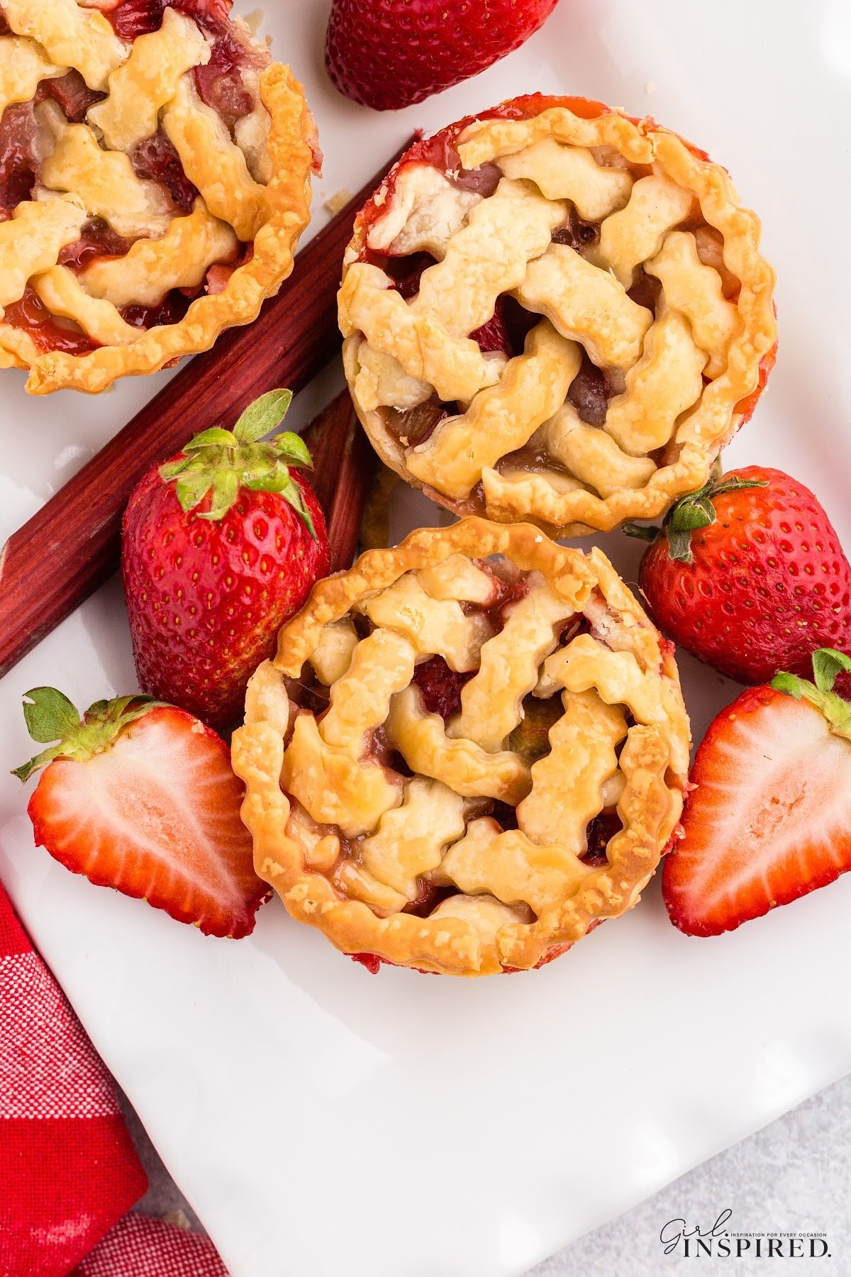Close up and top view of 3 strawberry rhubarb mini pies on a plate with whole strawberries surrounding.