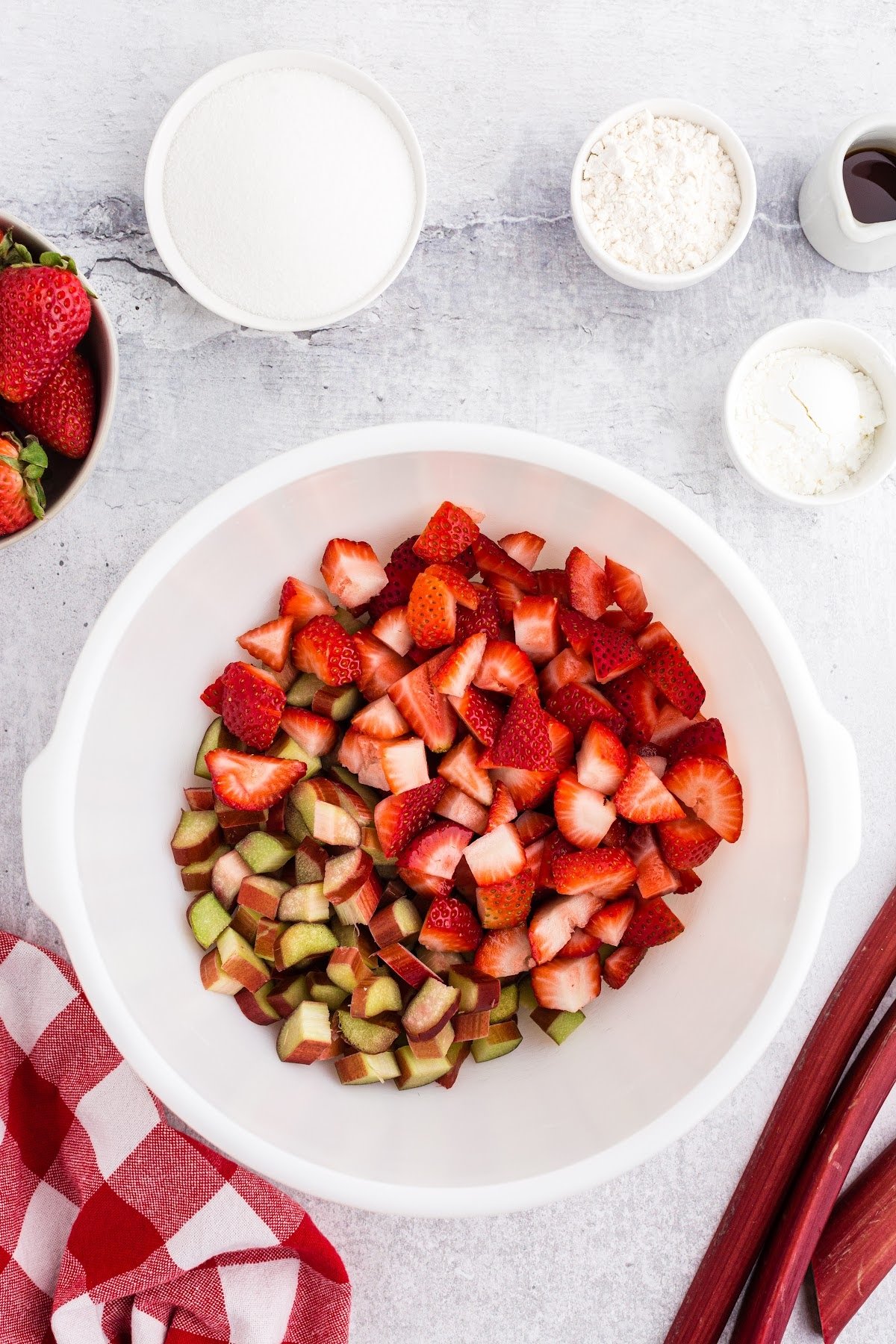 Added the strawberries and rhubarb to a bowl, with other ingredients in the background.