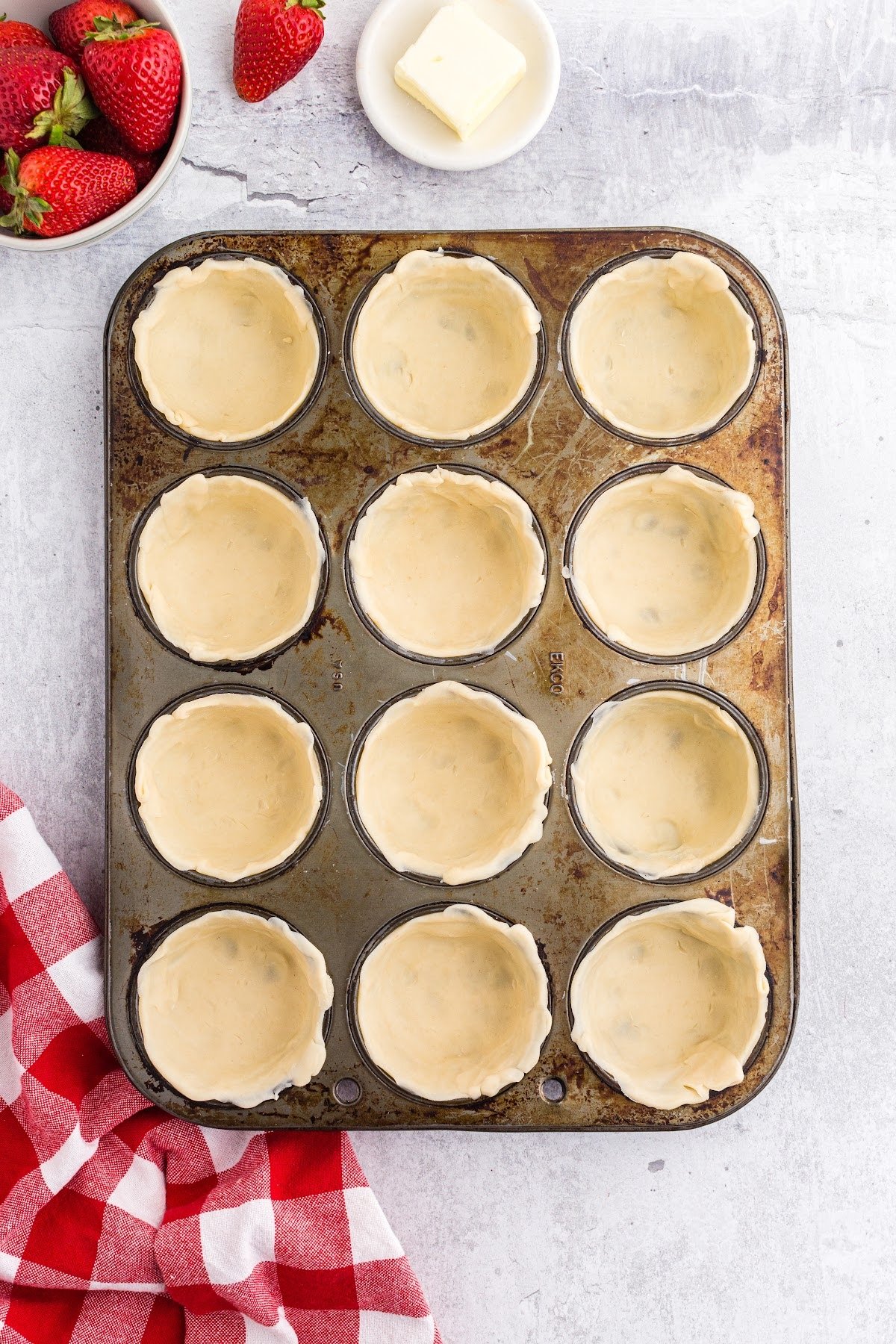 Pressing the cut pie dough into the muffin pan to form the base of the mini pies.