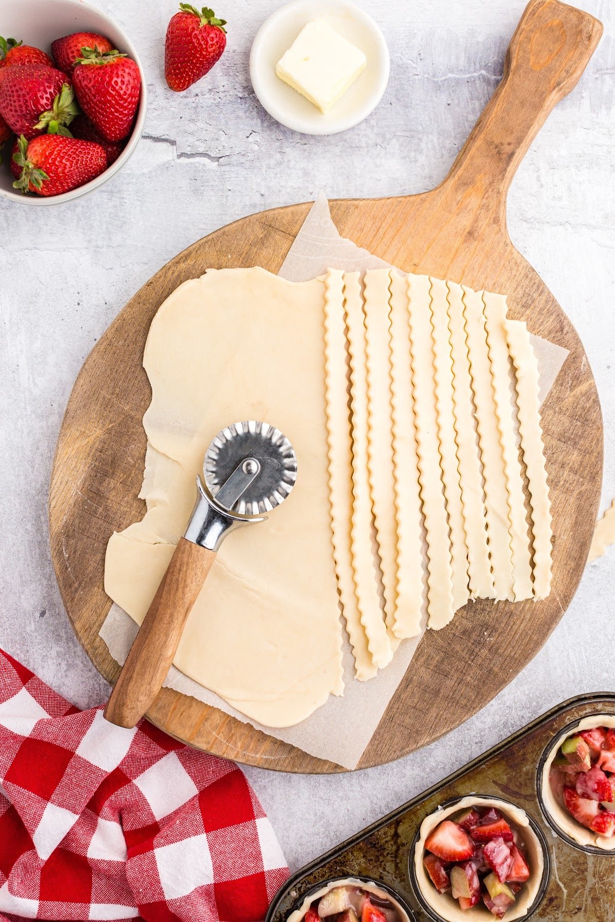 Cutting the pie dough into decorate strips on a cutting board with other ingredients in the background.