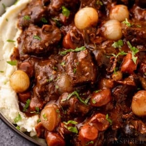 Beef bourguignon over mashed potatoes in serving bowl with herb garnish.