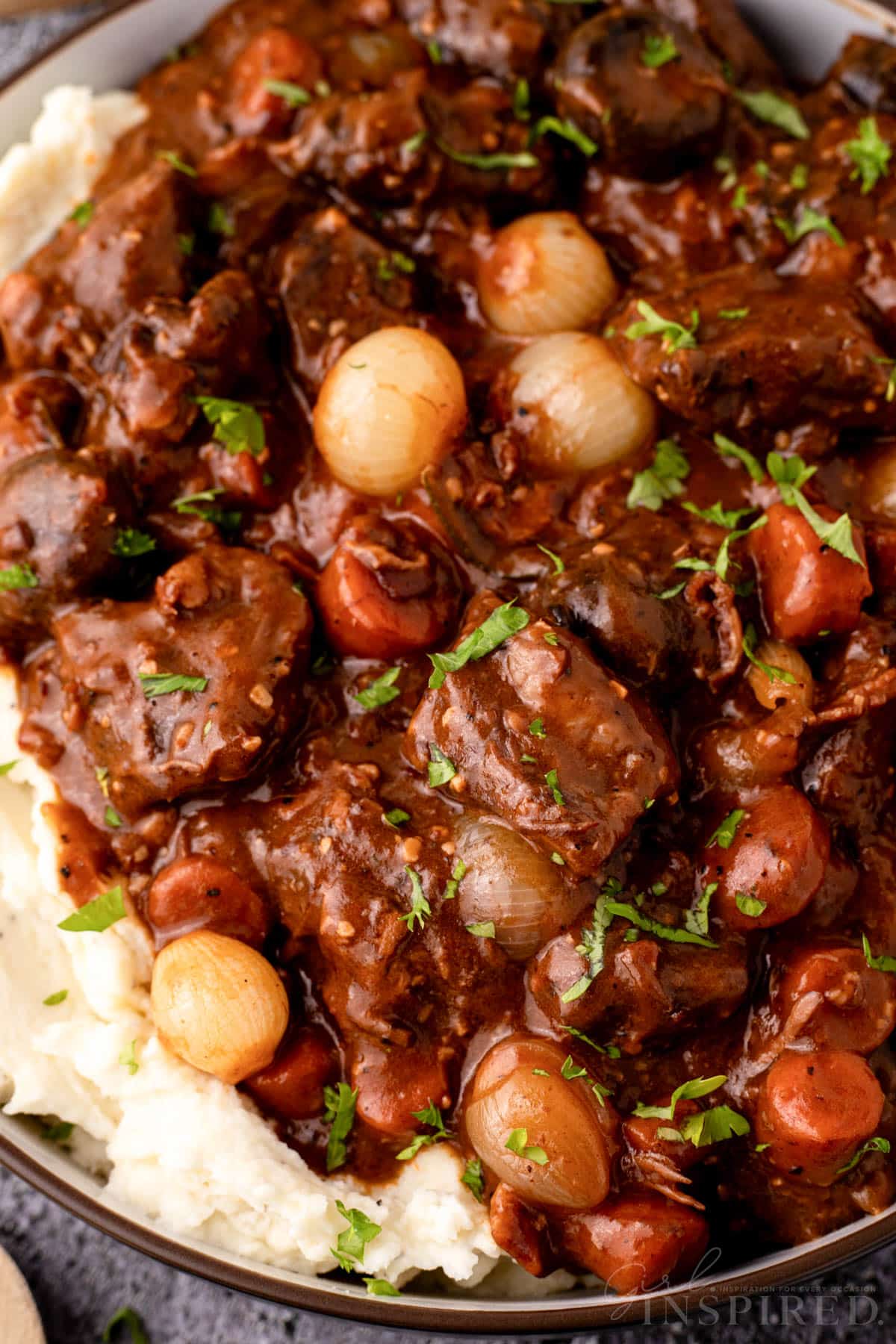 Beef bourguignon over mashed potatoes in serving bowl.