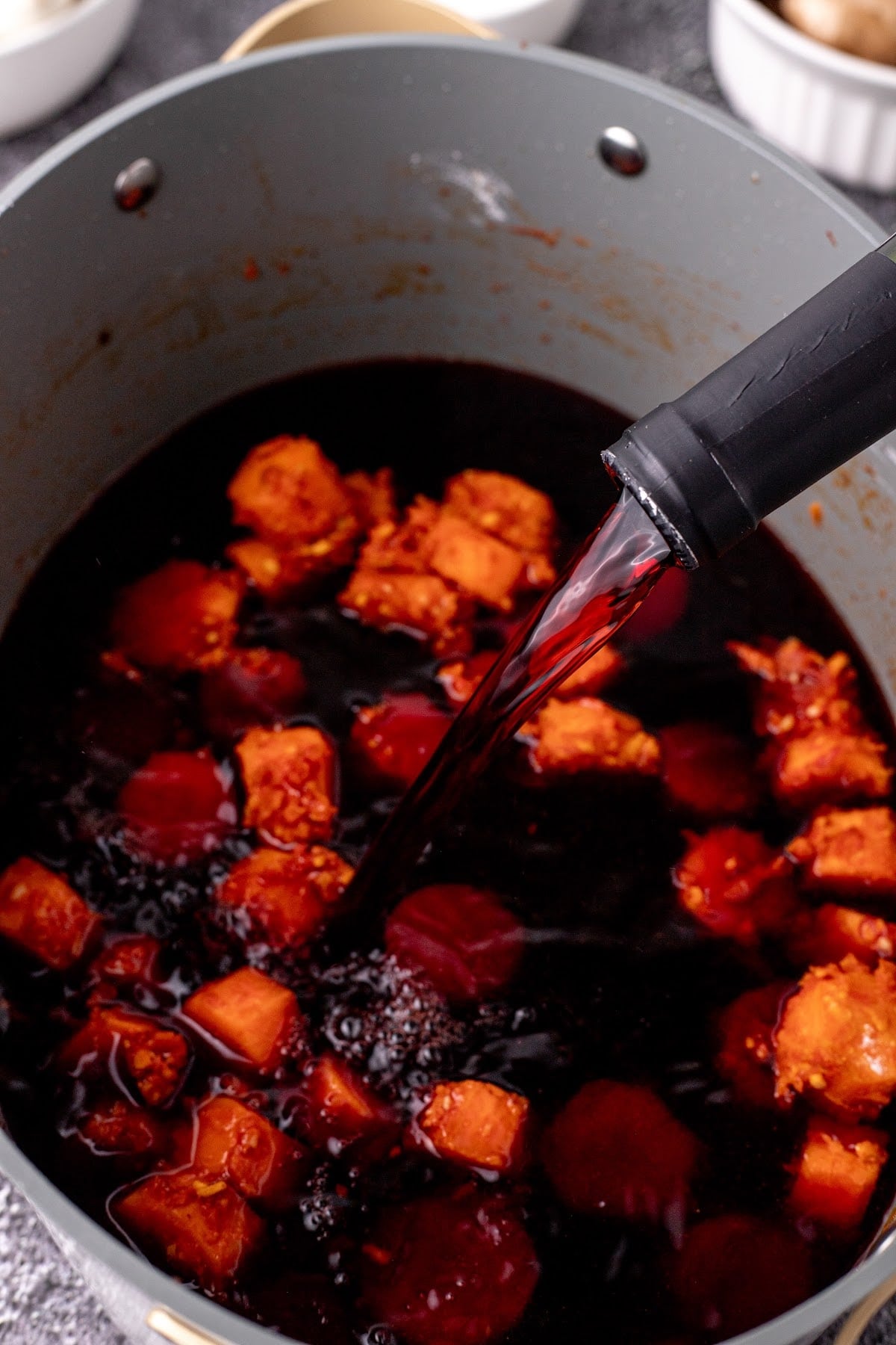 Pouring red wine into stockpot with carrots.