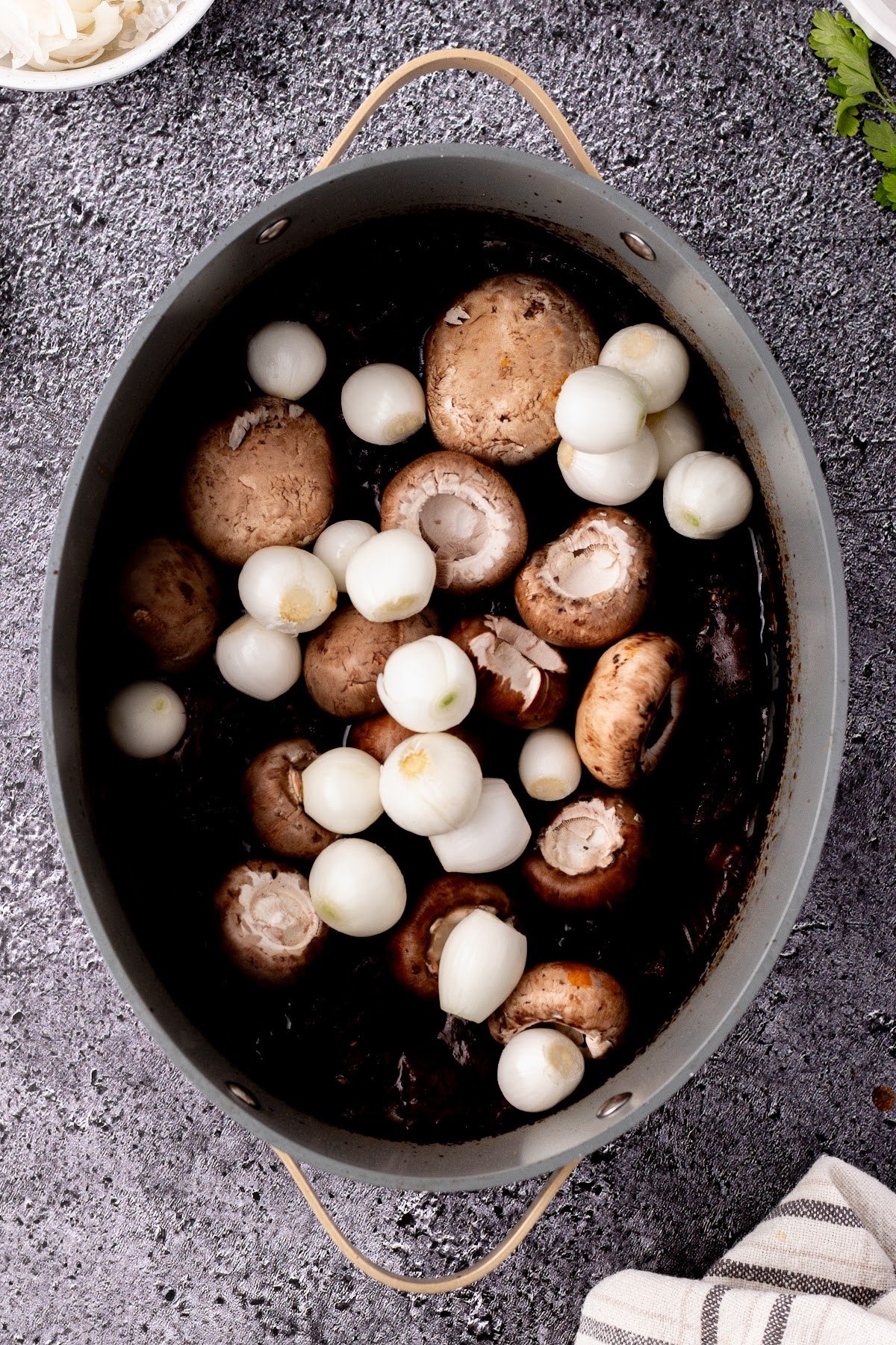 Mushrooms and pearl onions added over beef bourguignon in dutch oven.