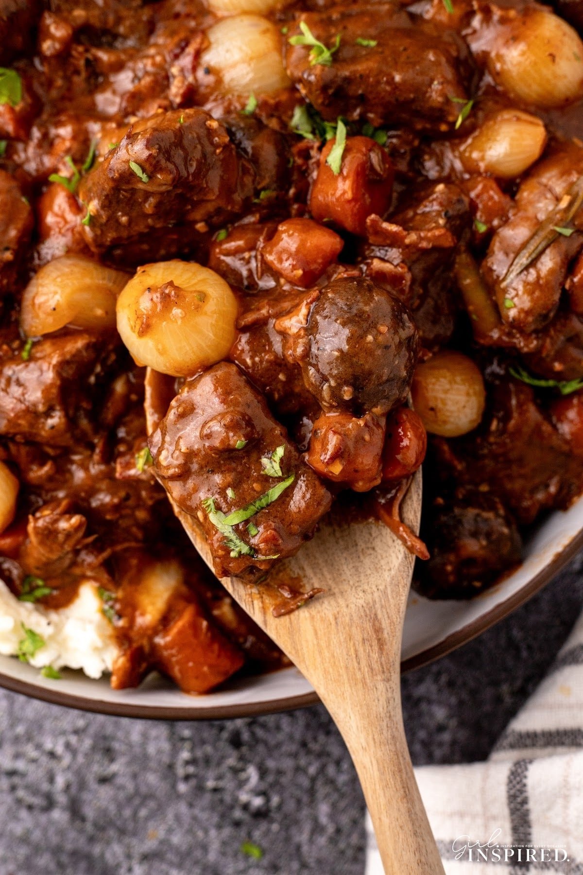 Wooden spoon scooping a serving of beef bourguignon from serving bowl.