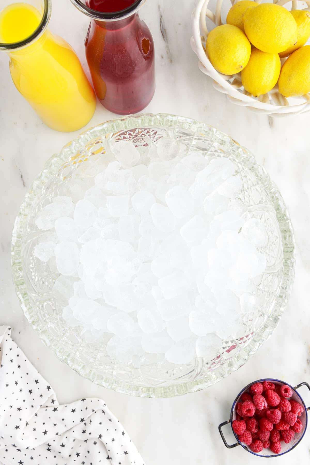 Large punch bowl filled with ice and berries, juice and lemons in the background.