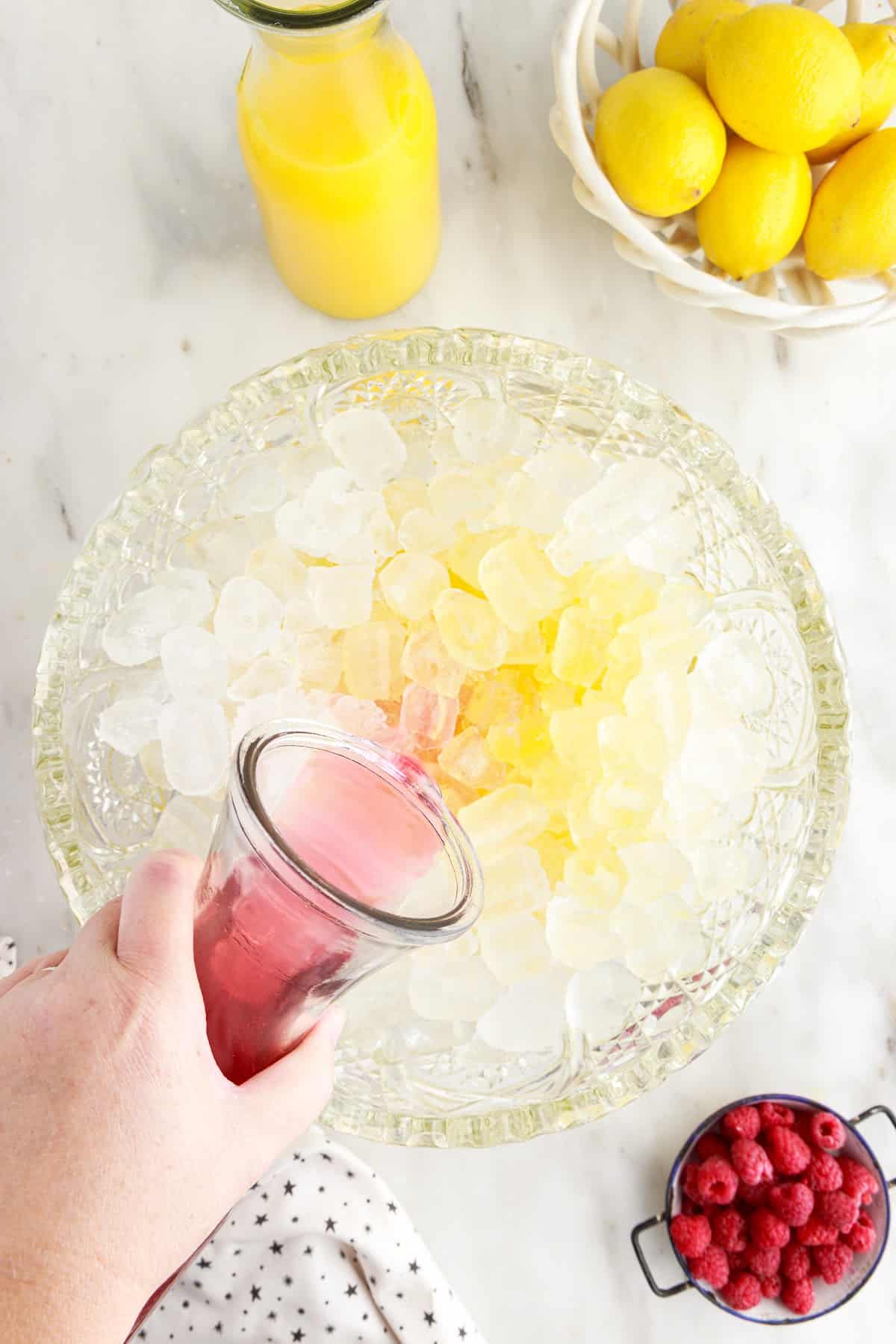 Adding in the punch into the bowl of ice and orange juice, with other ingredients in the background.