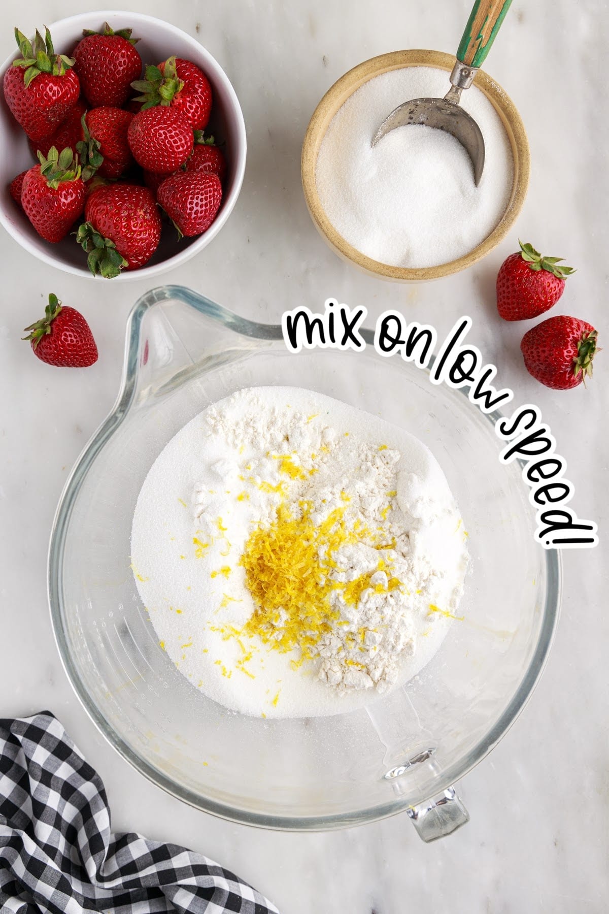 Added the shortbread ingredients to the bowl including the lemon zest, with strawberries and sugar in the background.