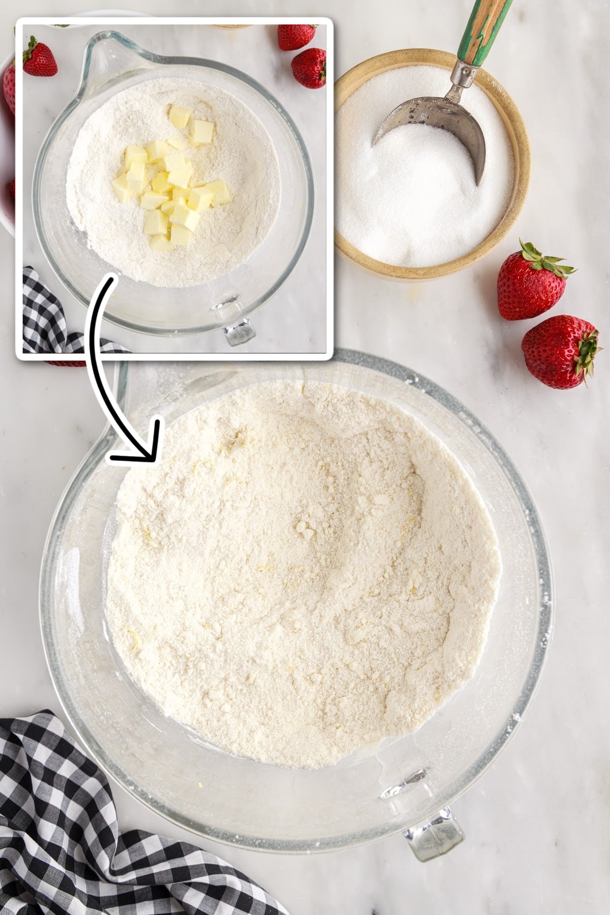 Adding cubes of cold butter to the flour mixture, with sugar and strawberries in the background.