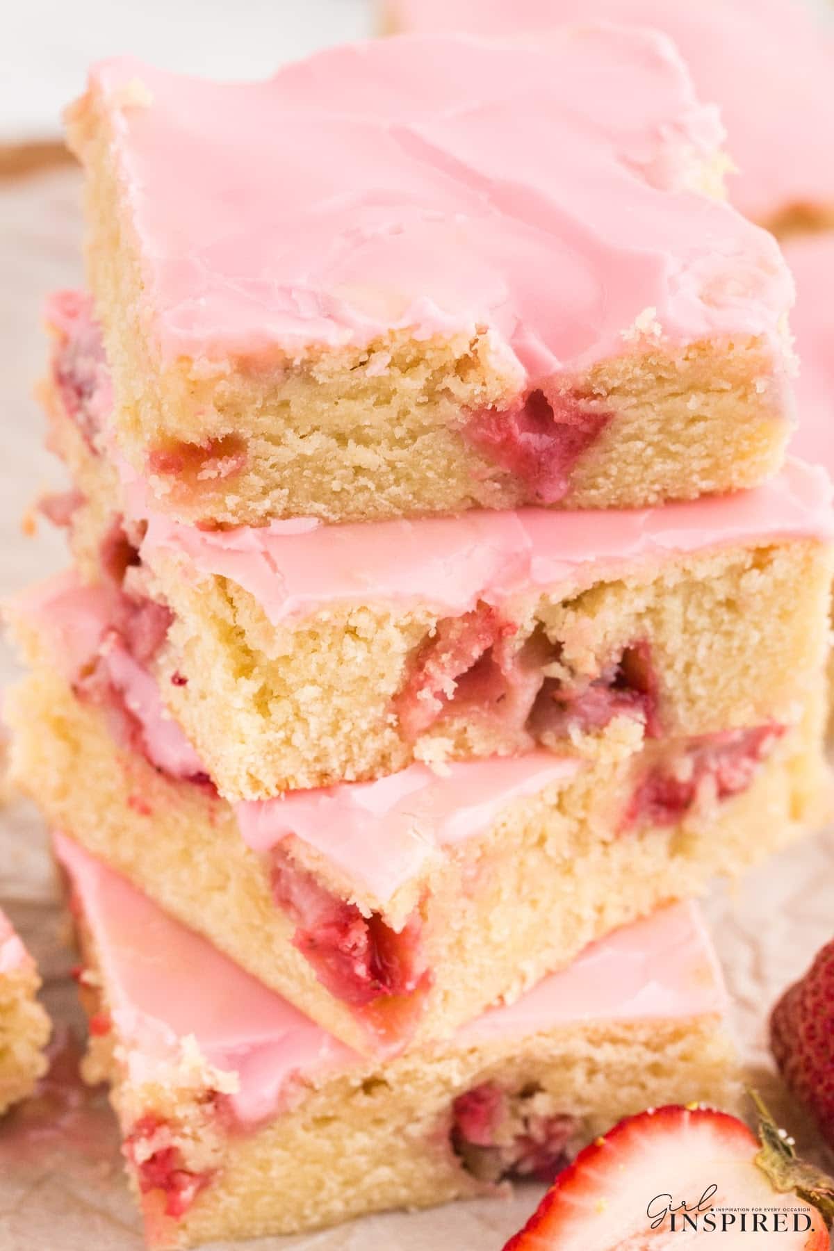 Tall stack of Strawberry Lemon Blondies on a plate showing the berries and brownie inside with pink frosting.