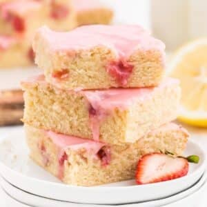 Tall stack of Strawberry Lemon Blondies on a plate showing the berries and brownie inside with pink frosting.