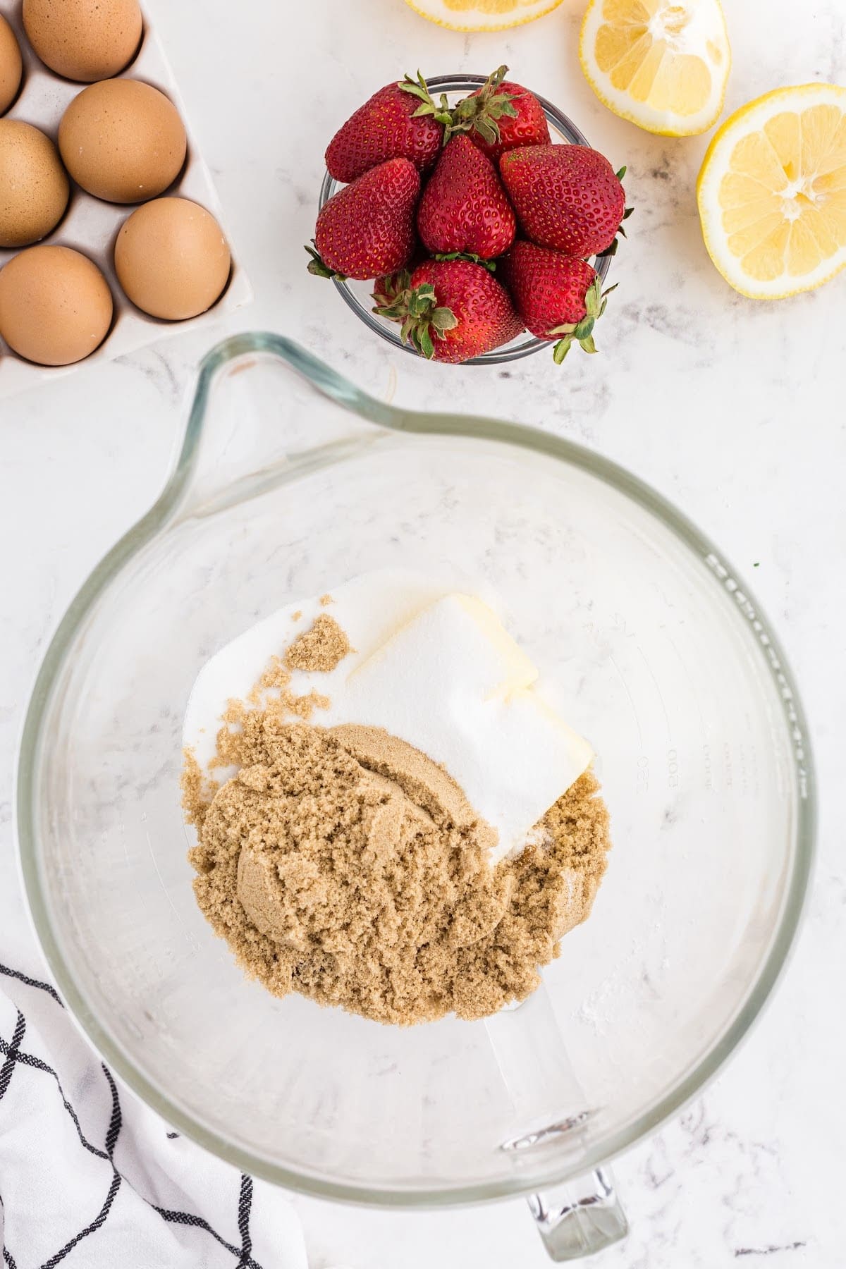 Placed the butter and sugars into a bowl to cream together until smooth, with eggs. lemons and strawberries in the background.