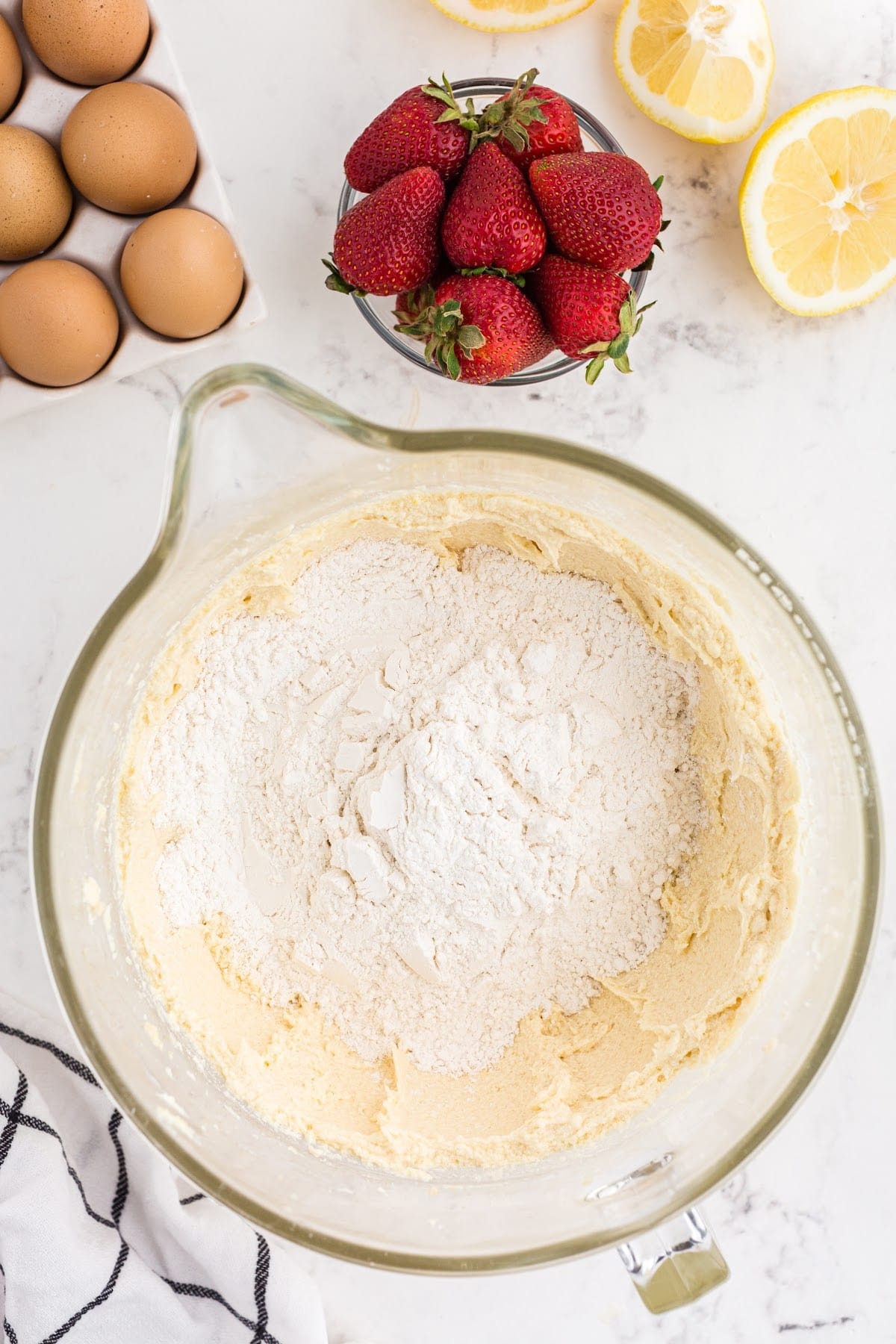 Mixing the dry ingredients together in a bowl, with eggs, lemons and strawberries in the background.