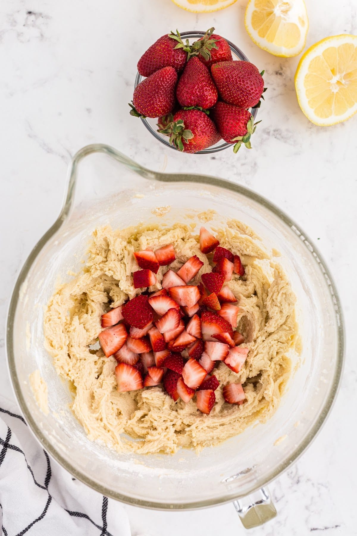 Mixing in the strawberries into the blondie batter, with strawberries and lemons in the background.