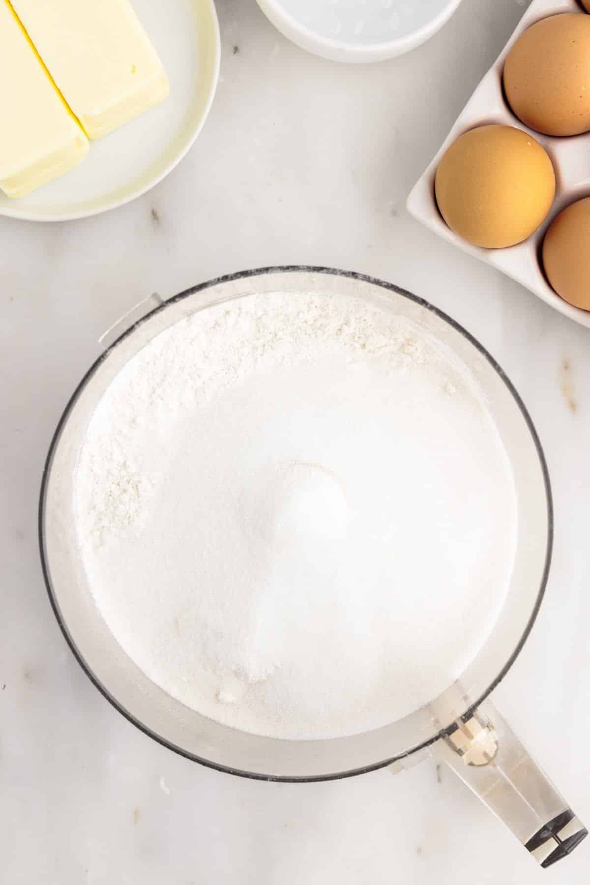 Bowl of a food processor with flour, sugar, and salt.