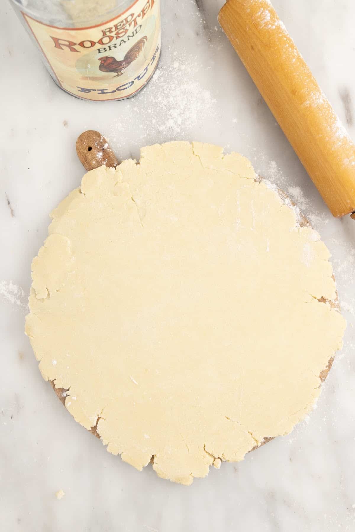 Pastry shell dough rolled out on a hard surface with a rolling pin.