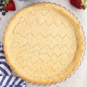 Golden brown Pate Sucree in tart pan on countertop with a few berries and a linen.