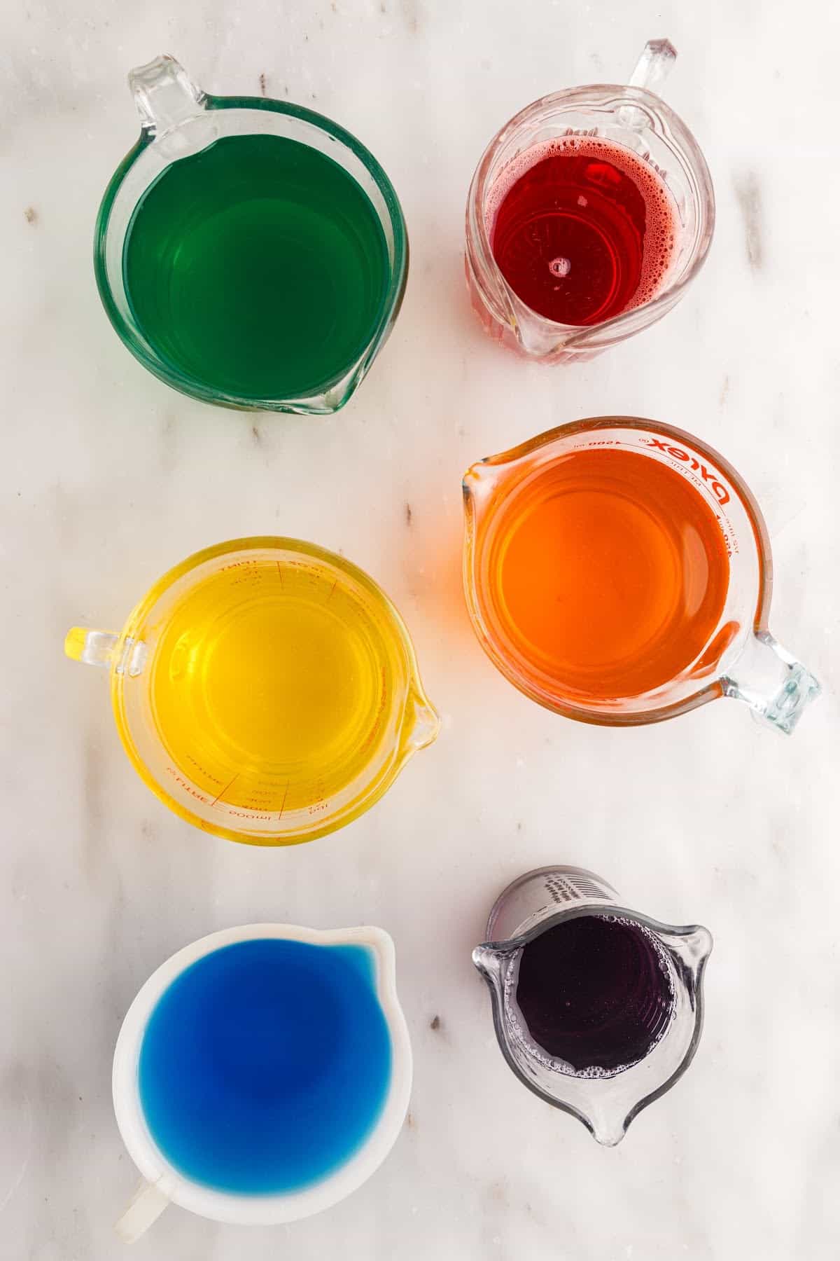 Cherry, orange, pineapple, lime, blue berry, and grape Jello dissolved in boiling water and placed in individual pouring jugs.