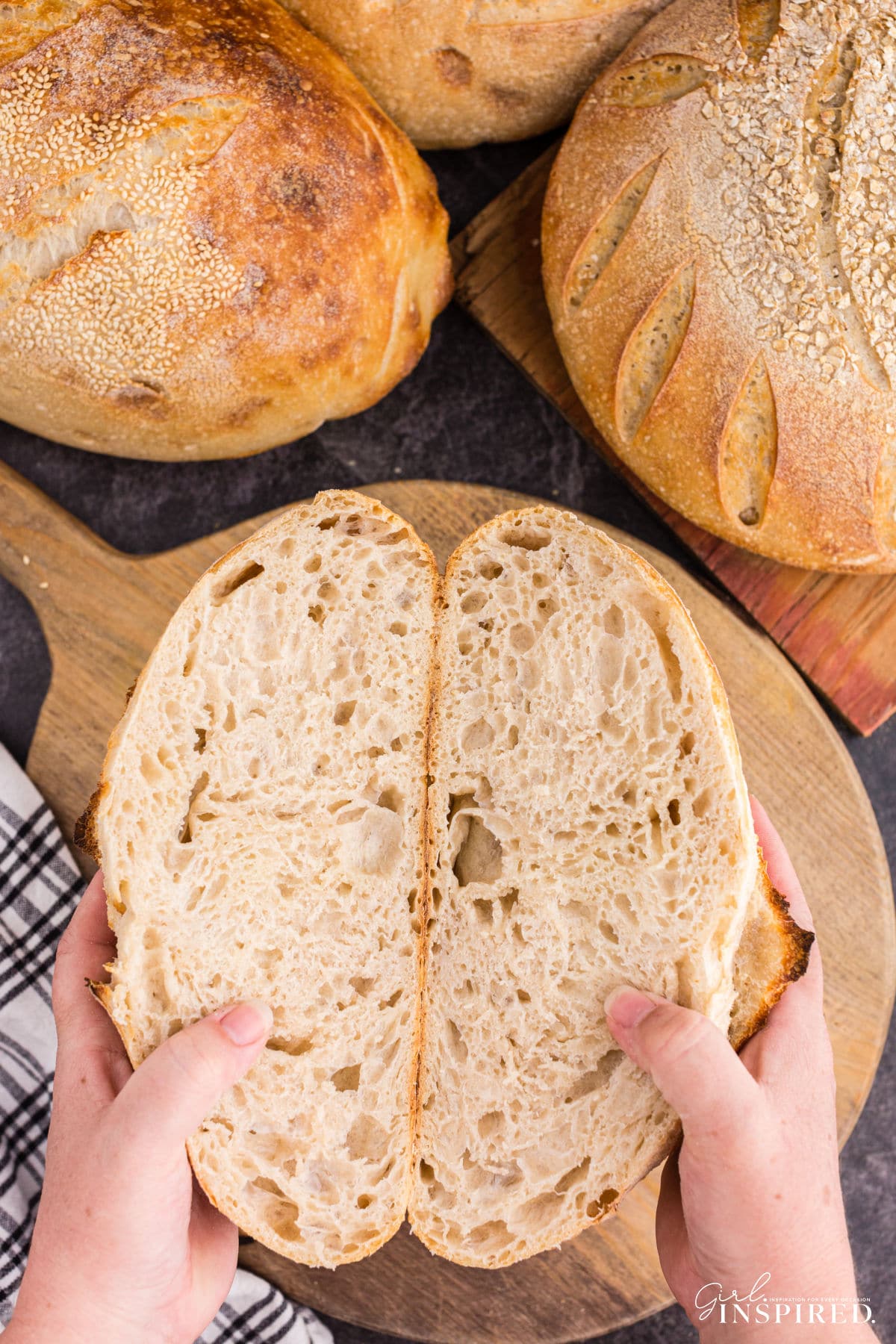 A set of hands holding the two halves of the basic sourdough bread loaf open over a cutting board.